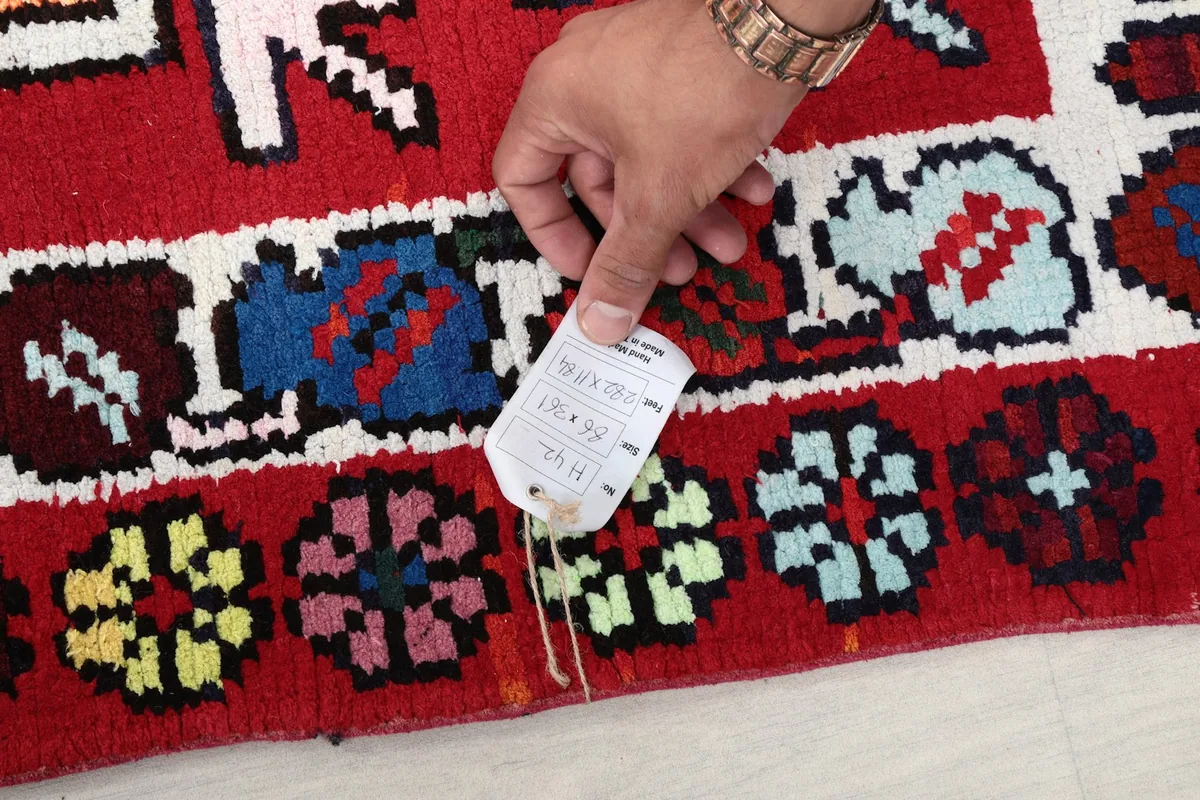 A hand holding a product tag over the rug, showing a close-up of the rug's pile and colors