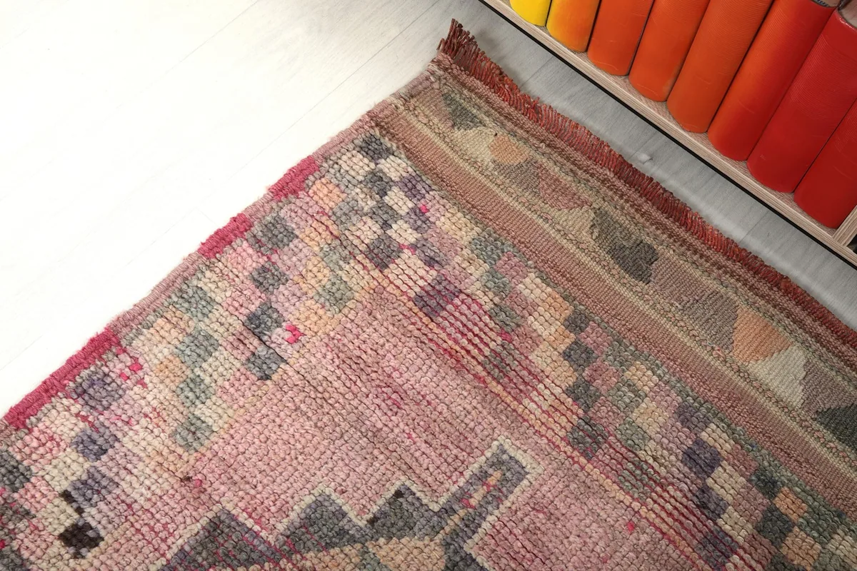 Angled detail of the rug's patterns and border near a bookshelf, highlighting color variations.
