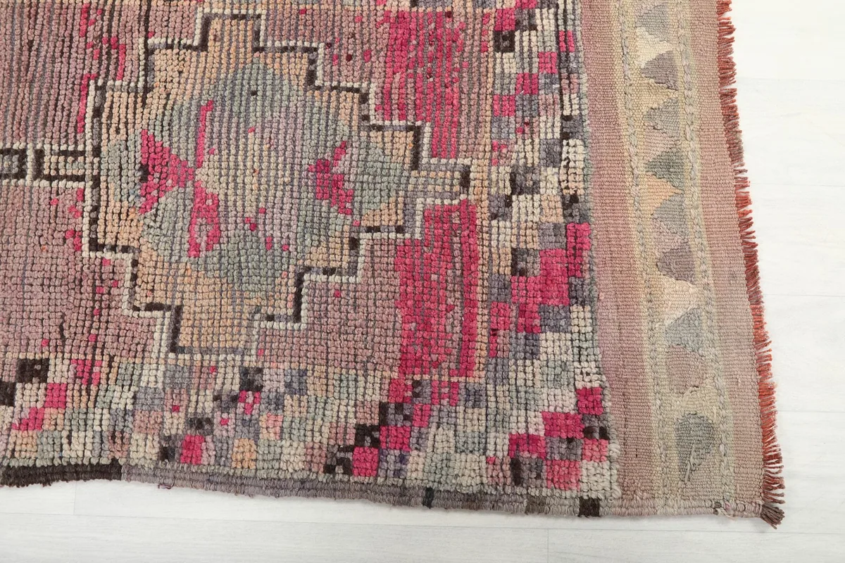 Detailed view of the rug's rose and pink geometric patterns and border texture.