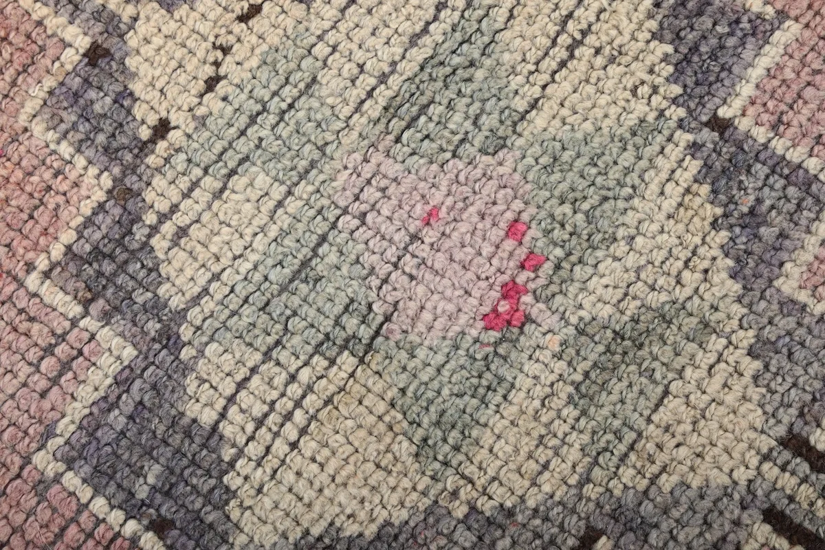 Macro shot showing the low wool pile and hand-knotted texture of the rug, with pink and blue threads.