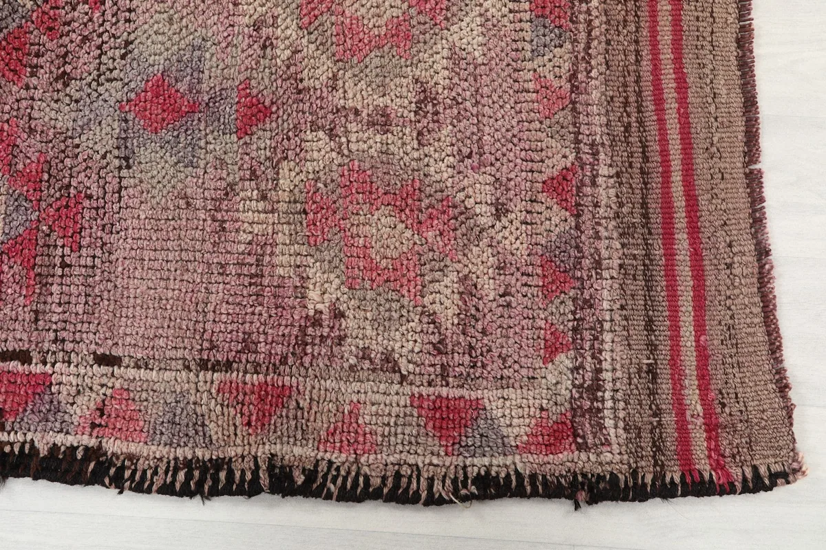 Detailed view of the rug's end, showing the hand-knotted texture, geometric border, and short fringe.