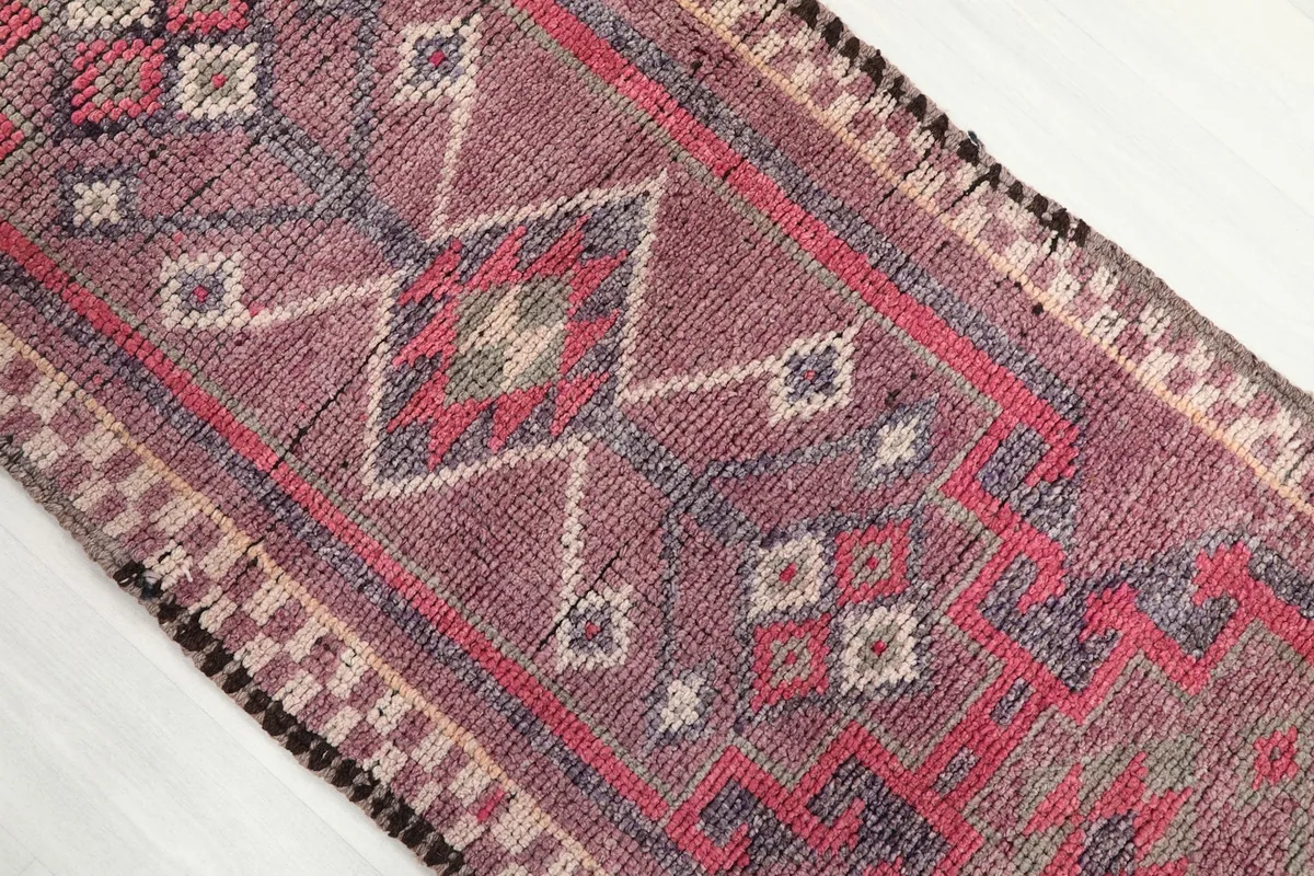 Close-up of the central geometric diamond motifs in rose, beige, and blue on the runner rug.