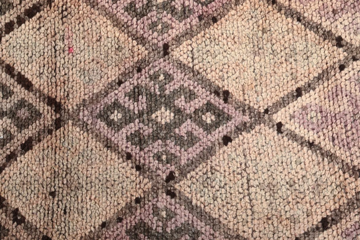 Macro detail of the wool pile, showing individual knots and the intricate geometric shapes in beige, purple, and gray.