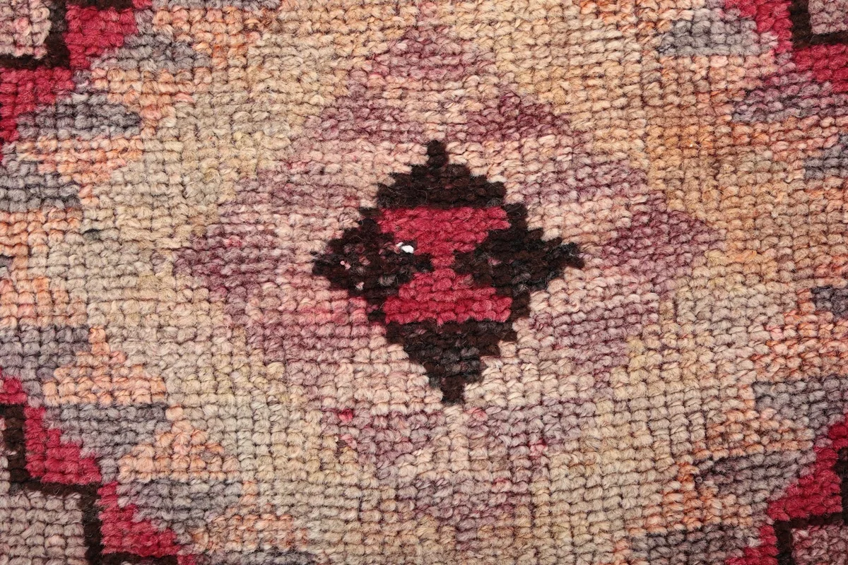 Close-up of the low wool pile texture and central motif in shades of rose, gray, and brown