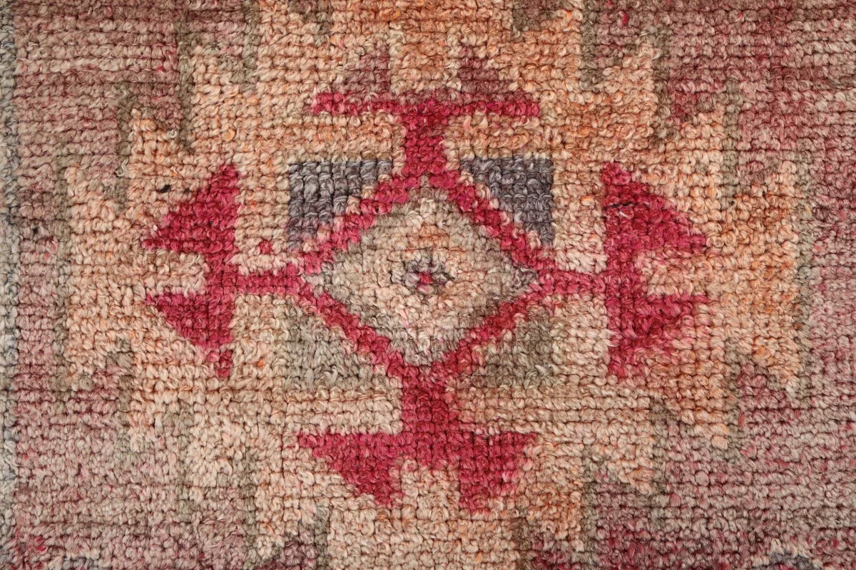 Macro shot of the wool pile, revealing the hand-knotted texture and faded rose and red tones.