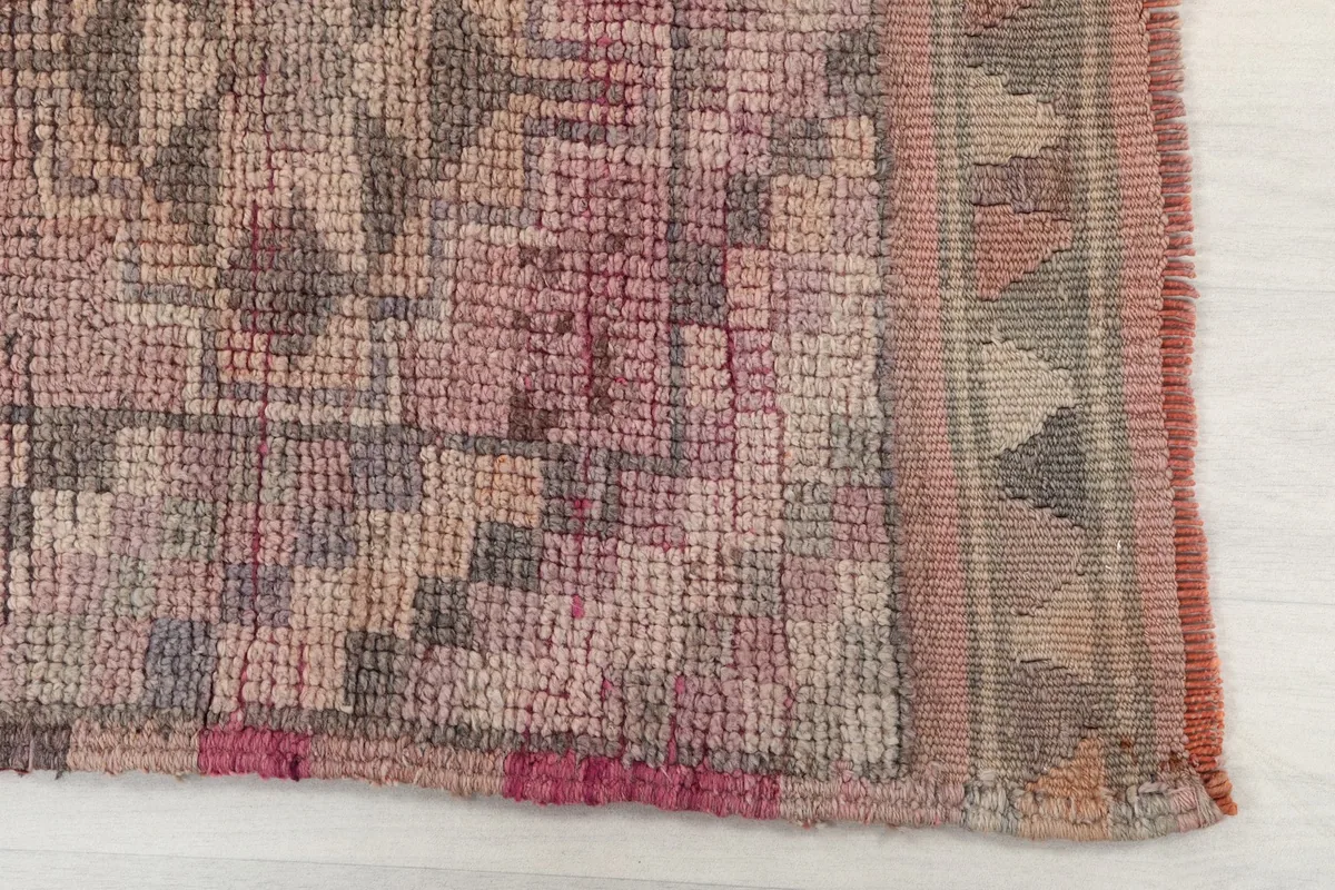 Detailed view of the hand-knotted wool pile and geometric motifs in rose, gray, and tan