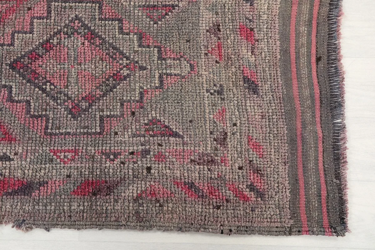 Close-up of the runner rug's end, highlighting the charcoal and pink geometric motifs and border