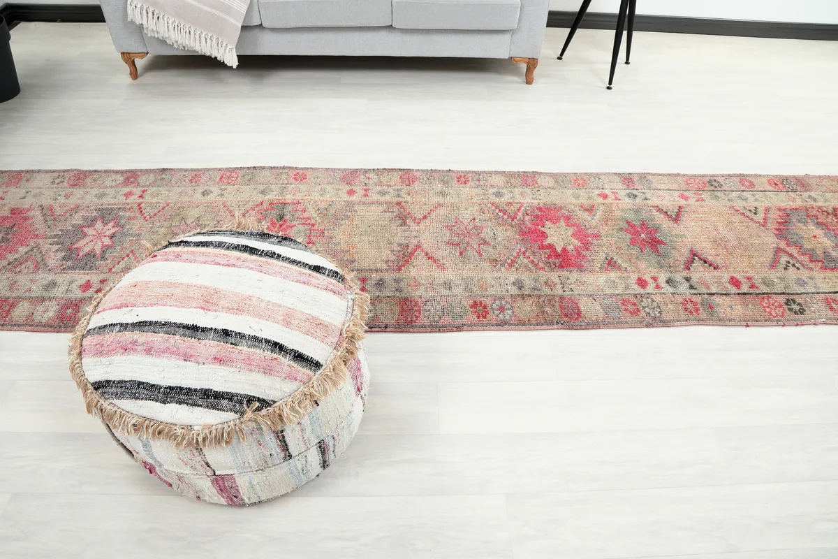Soft Rose Geometric Anatolian Runner in a living area, with a striped pouf in the foreground.