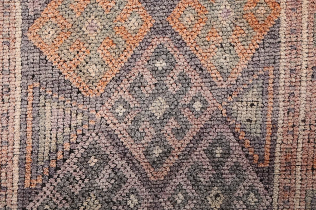 Extreme close-up of the hand-knotted wool pile, revealing the intricate weaving and distressed texture in gray and orange.