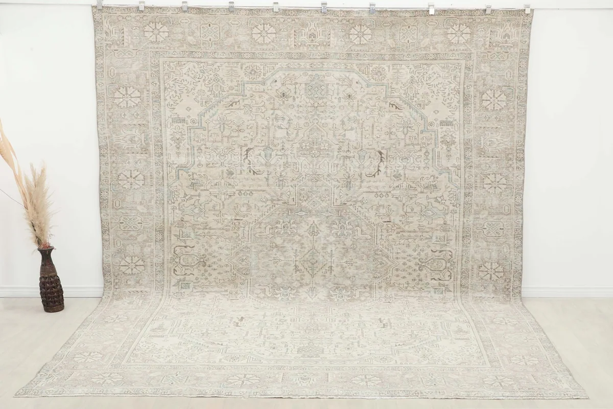 Large beige and gray Persian rug displayed against a wall in a spacious room setting.