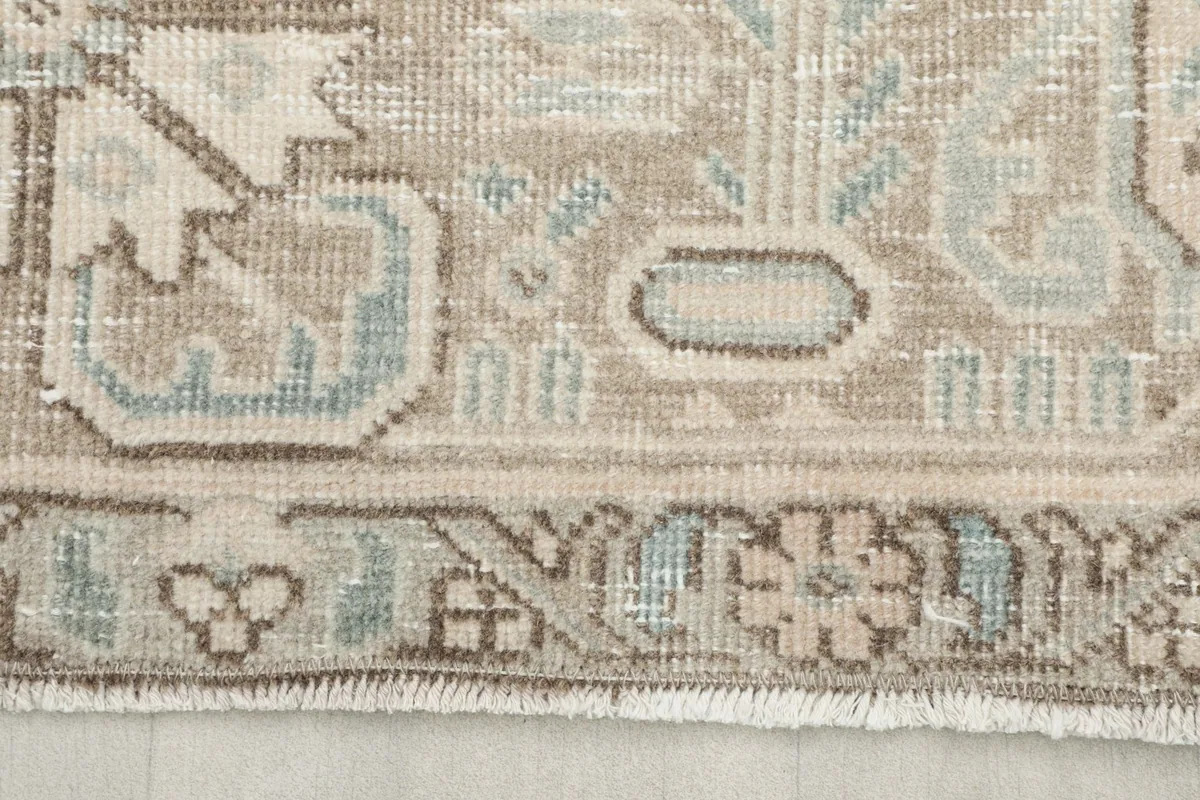 Close-up detail of the rug's border showing beige, gray, and light blue geometric patterns.