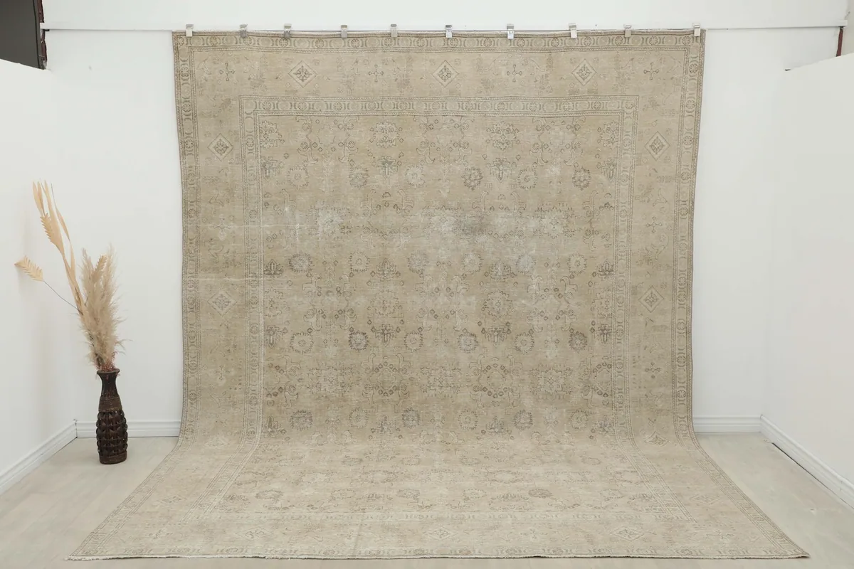 Large beige Persian rug draped against a wall, extending onto the floor, viewed from an angle