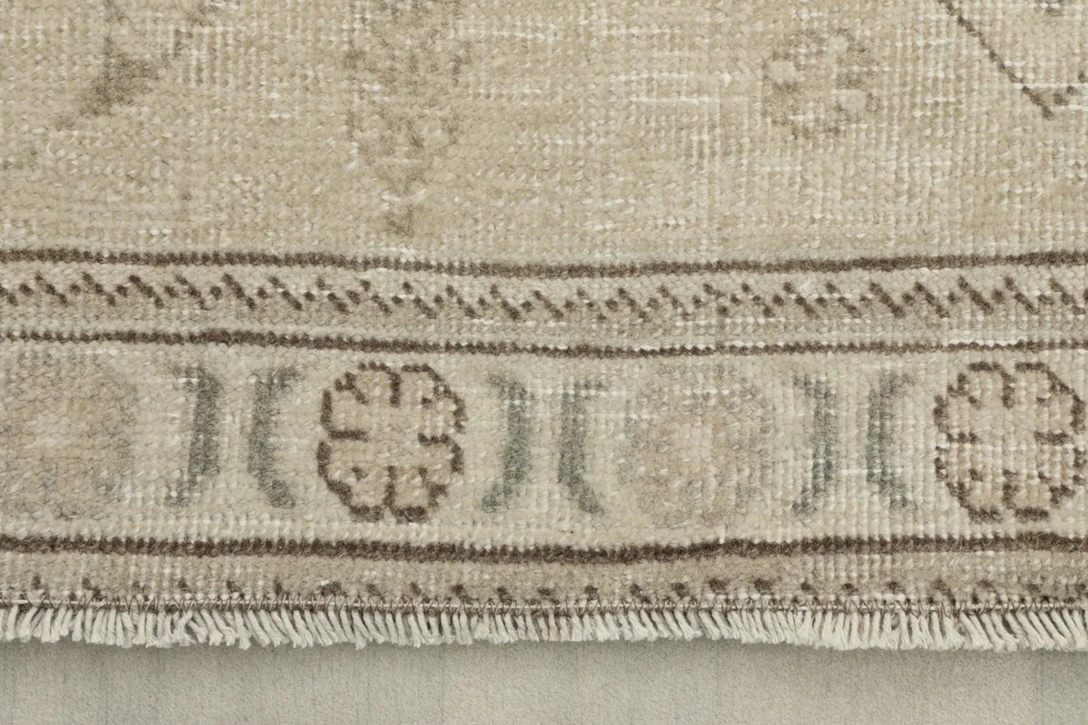 Close-up detail of the rug's border showing a gray and beige floral pattern and fringe