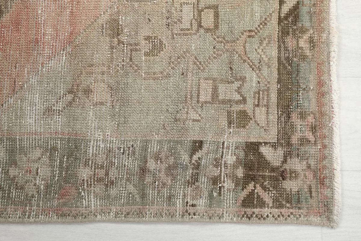 Detailed view of the corner of the rug, highlighting the faded gray and tan border motifs