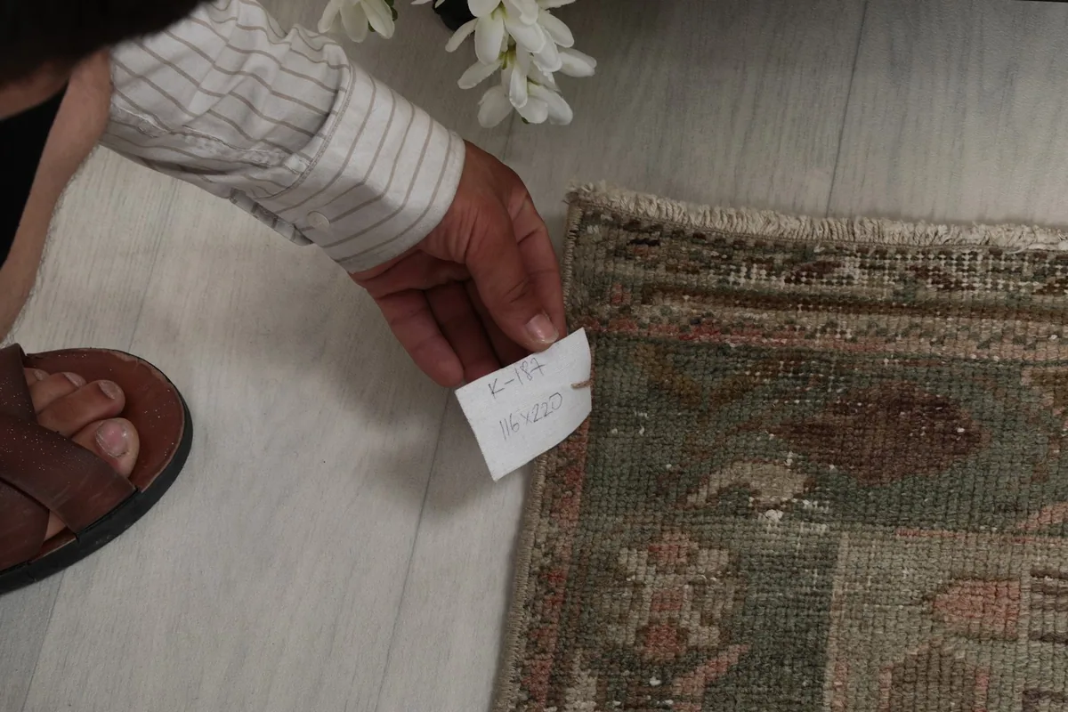 A hand holding a tag with rug information, showing the weave and border detail