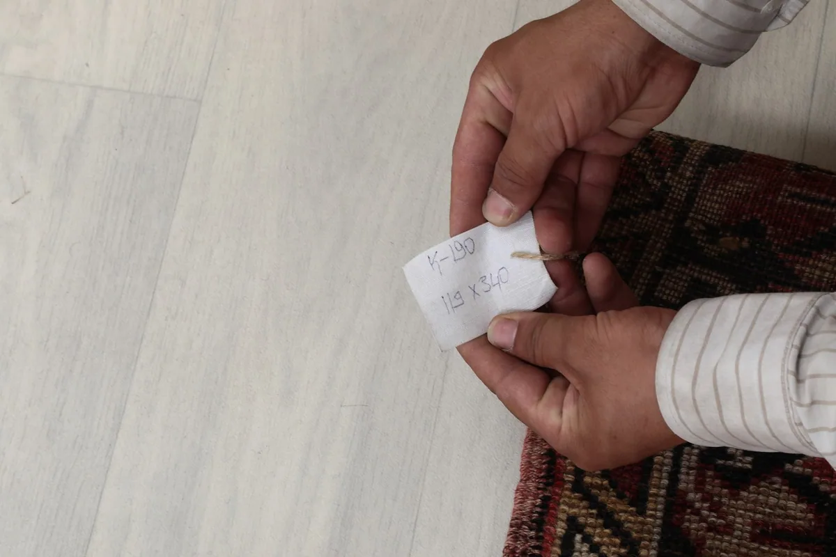 Hands holding a tag with the rug's dimensions '119 x 340 cm', confirming its size.
