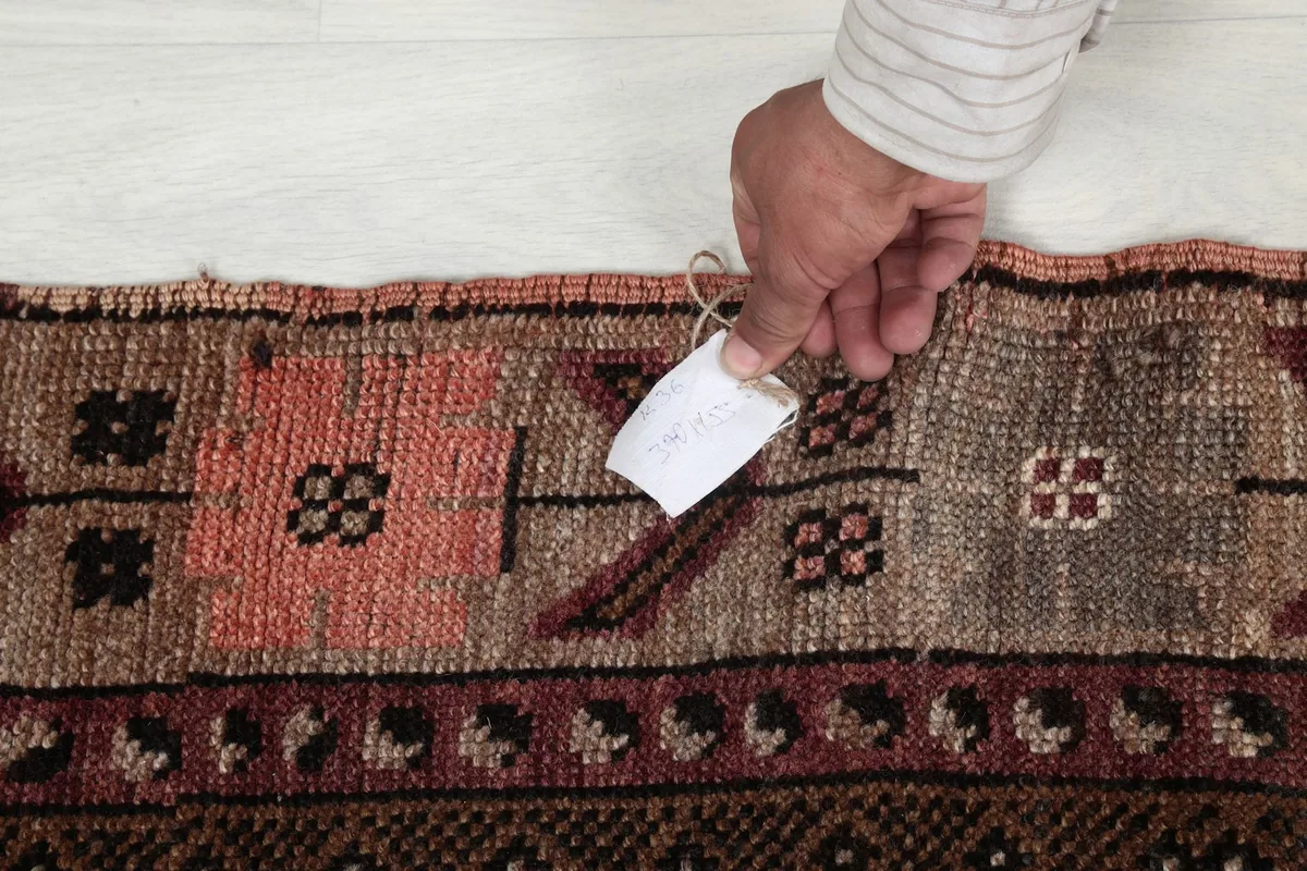 Hand holding a tag near the rug's fringe, showing the vintage wool texture
