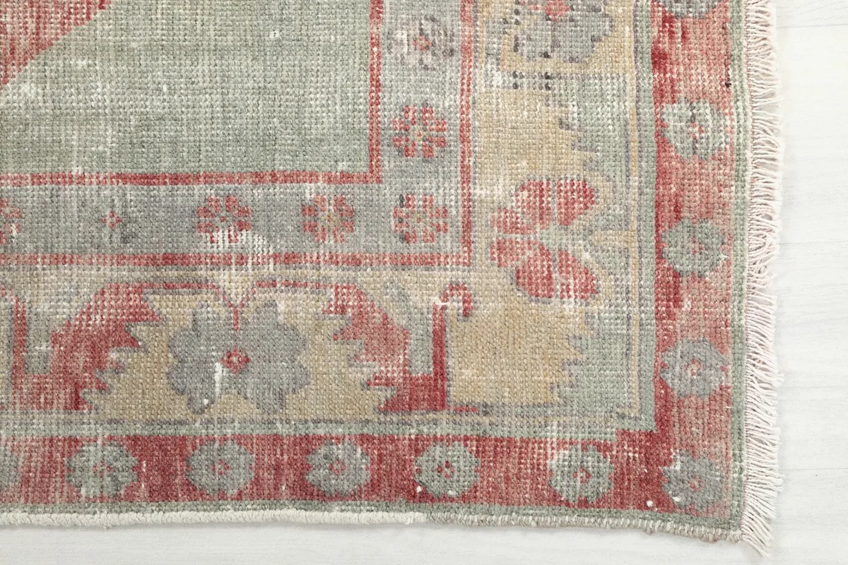 Detailed view of the rug's border, showcasing faded rust and gray floral-like motifs and fringe.
