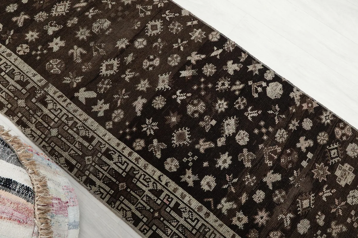 Overhead angle view of the brown runner rug, emphasizing the scattered tribal motifs.
