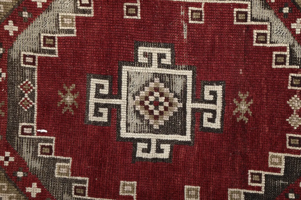 Close-up of a central geometric motif within the red field, showing the fine knotting and subtle wear.