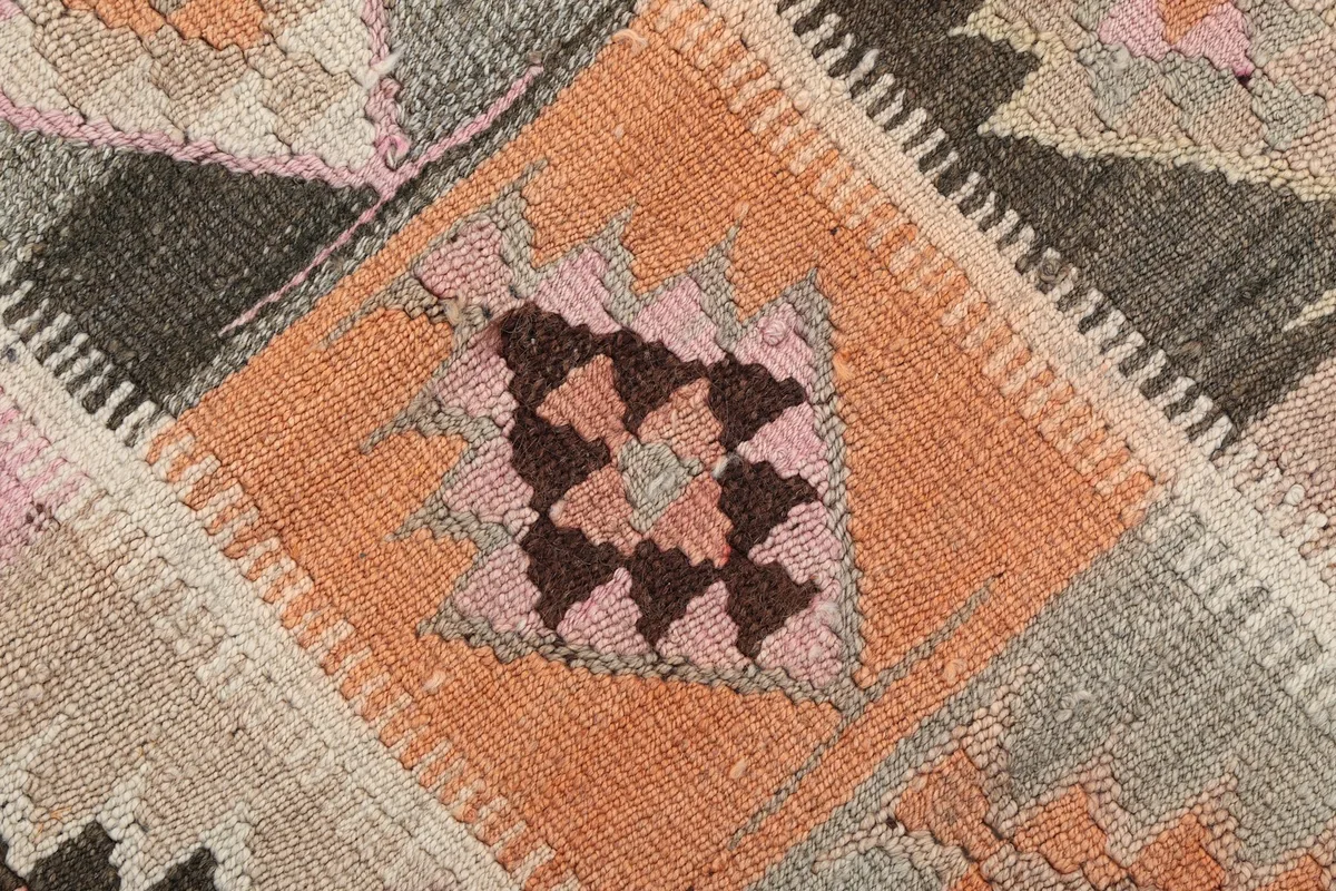 Close-up of an orange square with a tribal motif, revealing the wool pile and knotting detail.