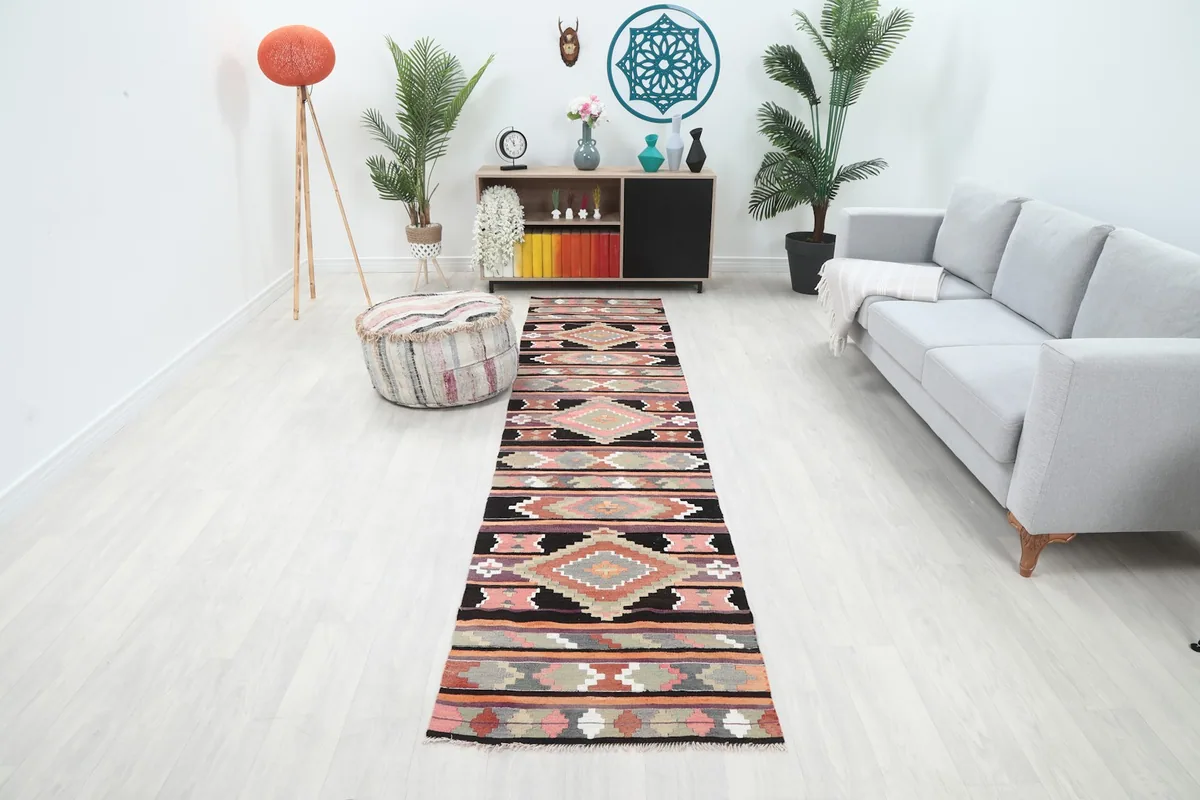 A 2'7" x 11'2" black, pink, and orange geometric runner rug laid in a modern hallway with light wood floors.