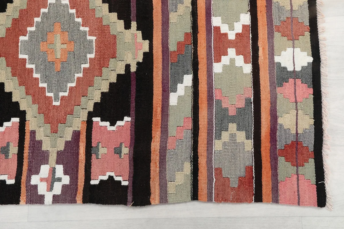 Detailed view of the hand-knotted wool pile showing geometric patterns in black, pink, orange, rust, gray, and purple.