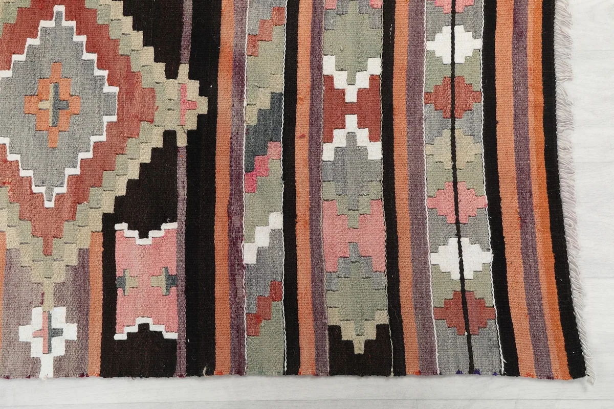 Detailed view of the hand-knotted wool pile and the intricate geometric motifs in black, rust, and gray