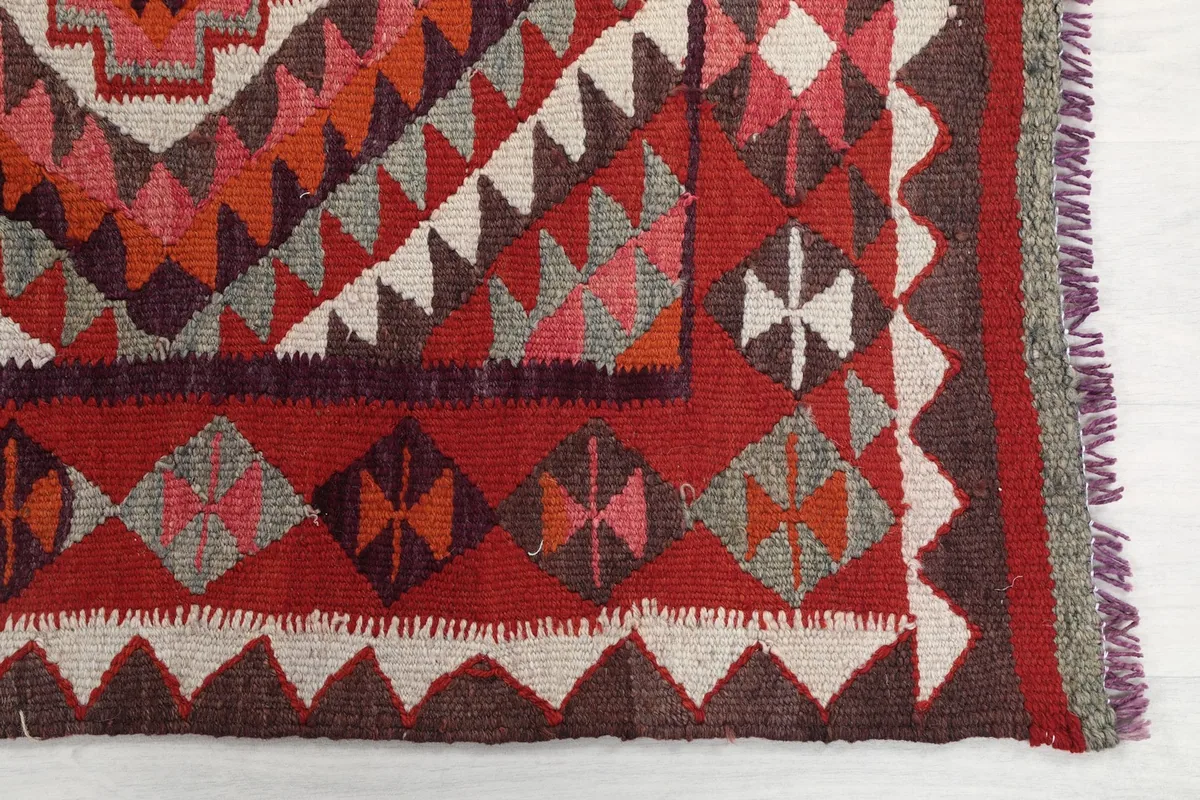 Detail of the rug's end, showing red, gray, and brown geometric motifs and fringe