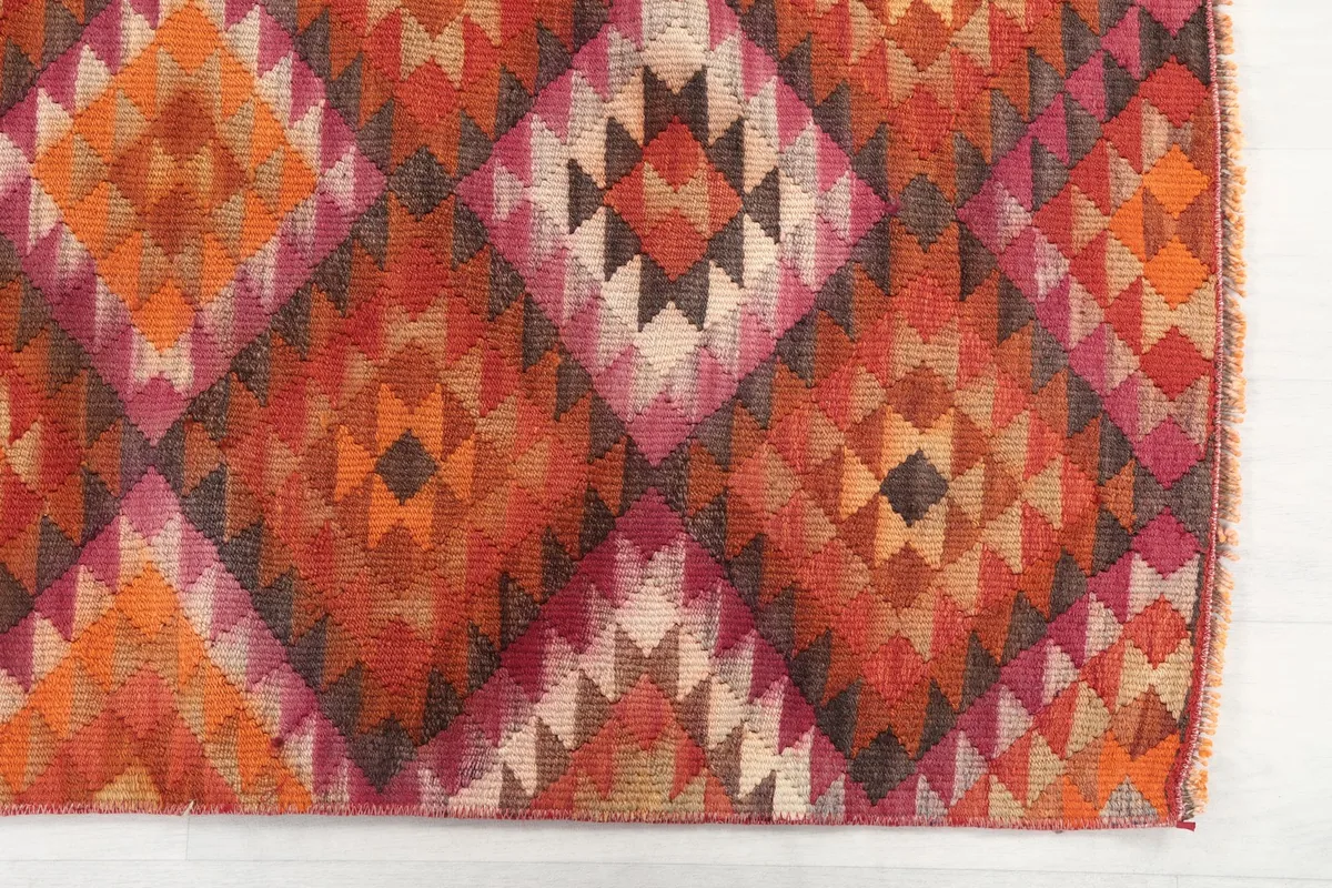 Detailed view of the orange, rust, and pink geometric patterns on the vintage runner rug