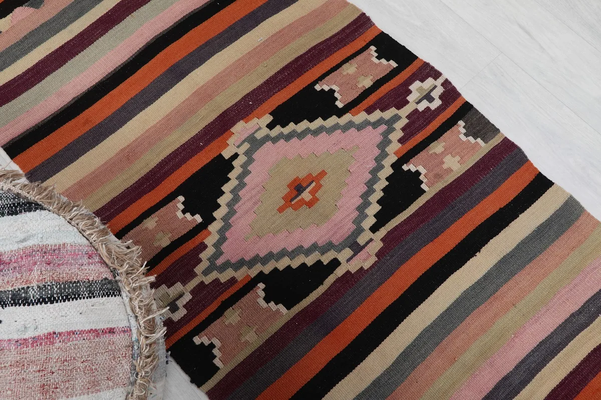 Angled view of the rug's geometric motif and surrounding stripes, next to a striped pouf.