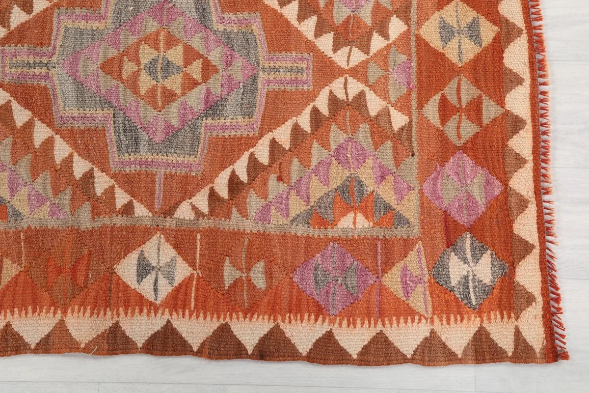 Close-up of the rug's end, revealing the intricate geometric patterns in orange, pink, gray, and beige