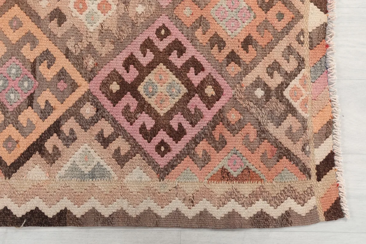Detailed view of the rug's hand-knotted construction and tribal diamond motifs in rose, orange, and brown.