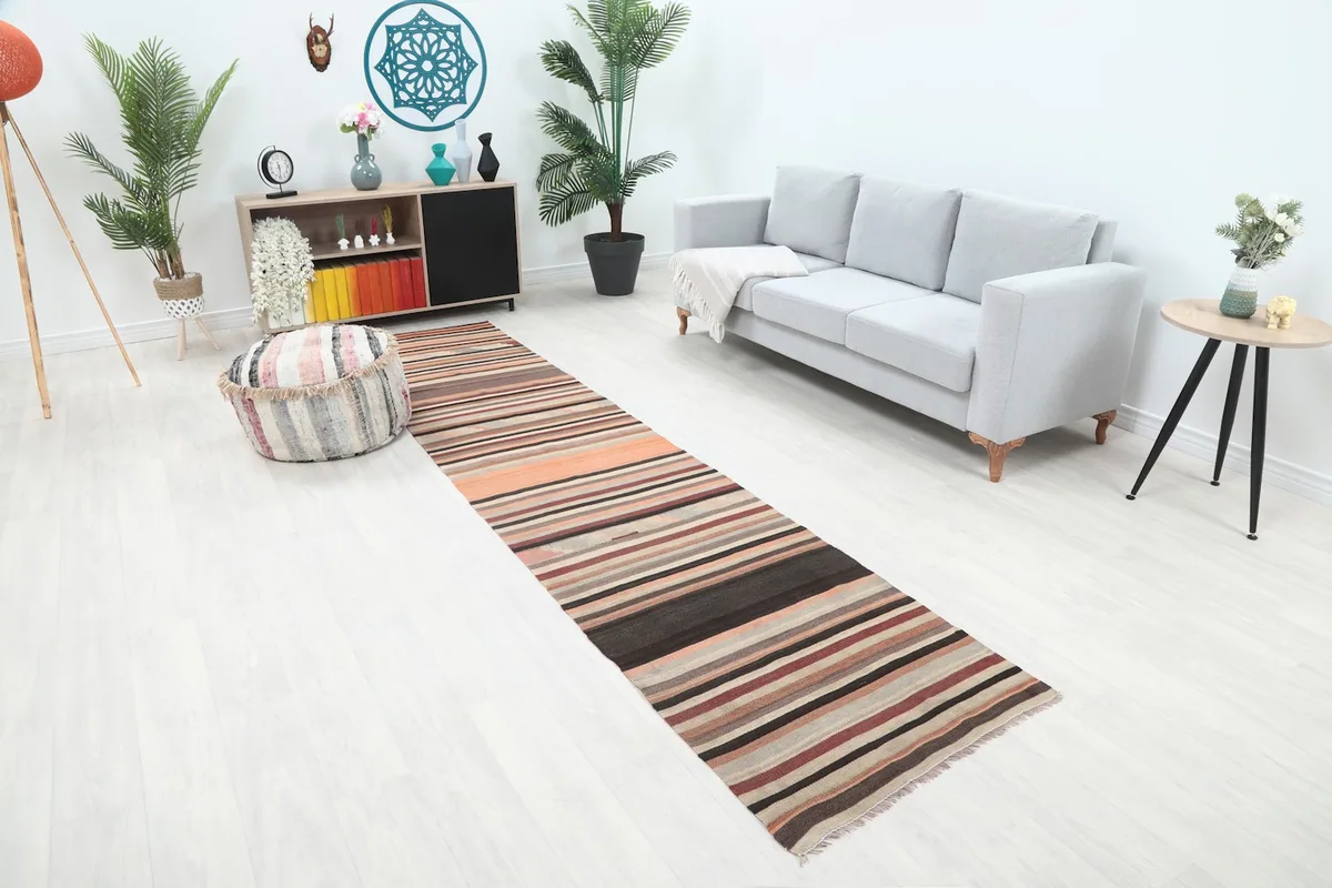 Angled view of the orange, red, and brown striped runner in a bright room with a light gray sofa and ottoman.