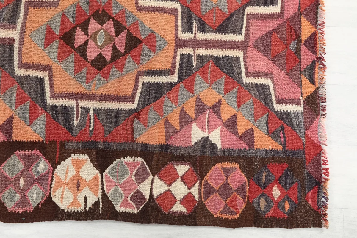 Detailed view of the rug's end with rust, gray, and pink geometric motifs and circular border elements.