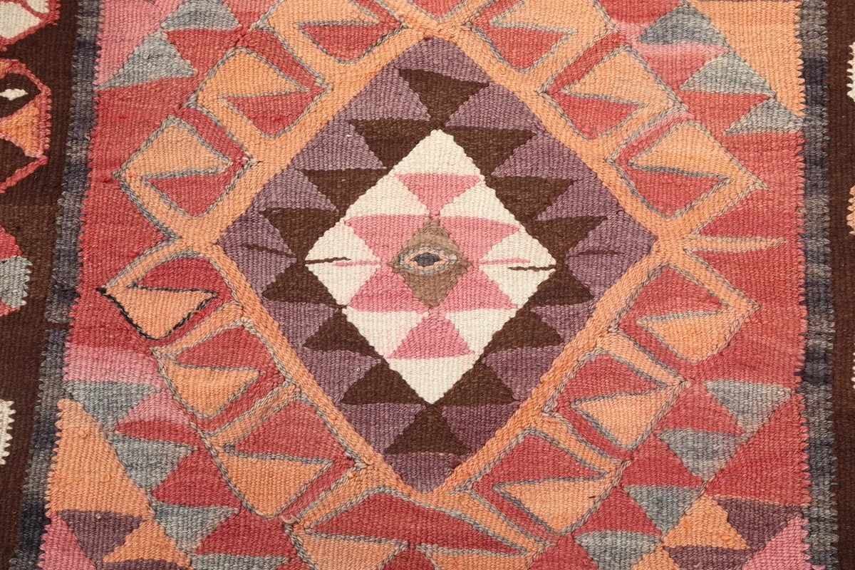 Close-up of a central diamond motif with pink, brown, and ivory colors, showcasing the hand-knotted wool pile.