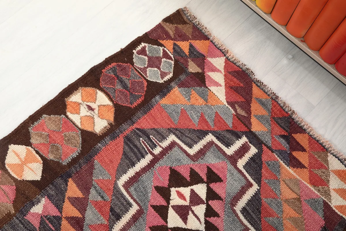 Corner detail of the rug showing the brown border with circular patterns and the main rust geometric field.