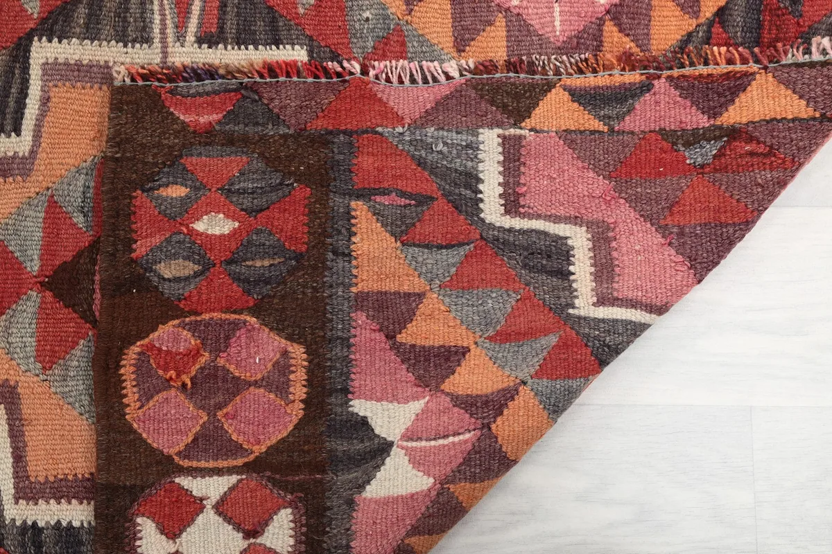 Close-up of a folded section, showing the rug's thickness and the interplay of rust, pink, and orange colors.