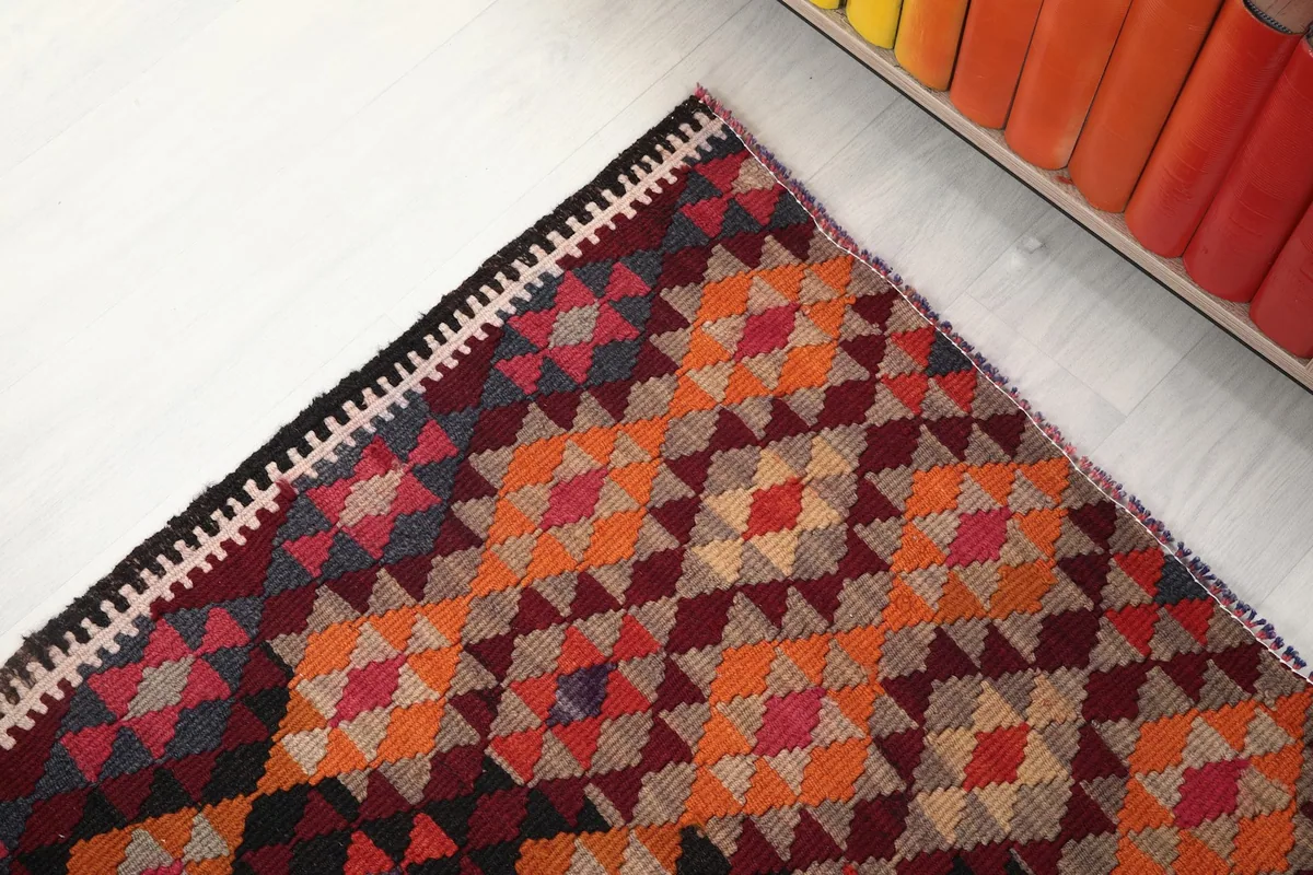Corner view of the runner rug showing the vibrant orange and red geometric patterns near a bookshelf.