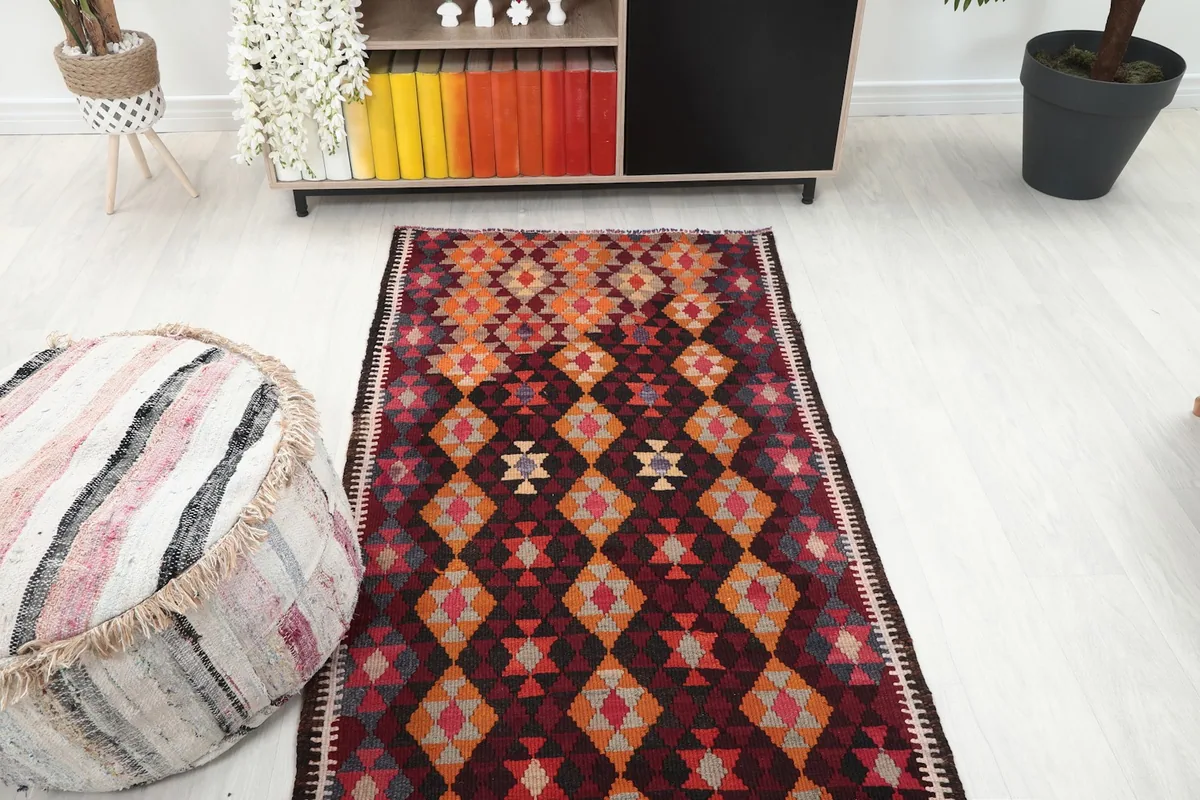 Overhead view of the red geometric runner rug in a room, with an ottoman and shelving unit.