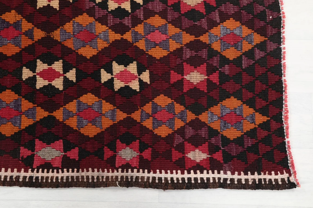 Detailed view of the red, orange, and beige geometric patterns and border on the rug.