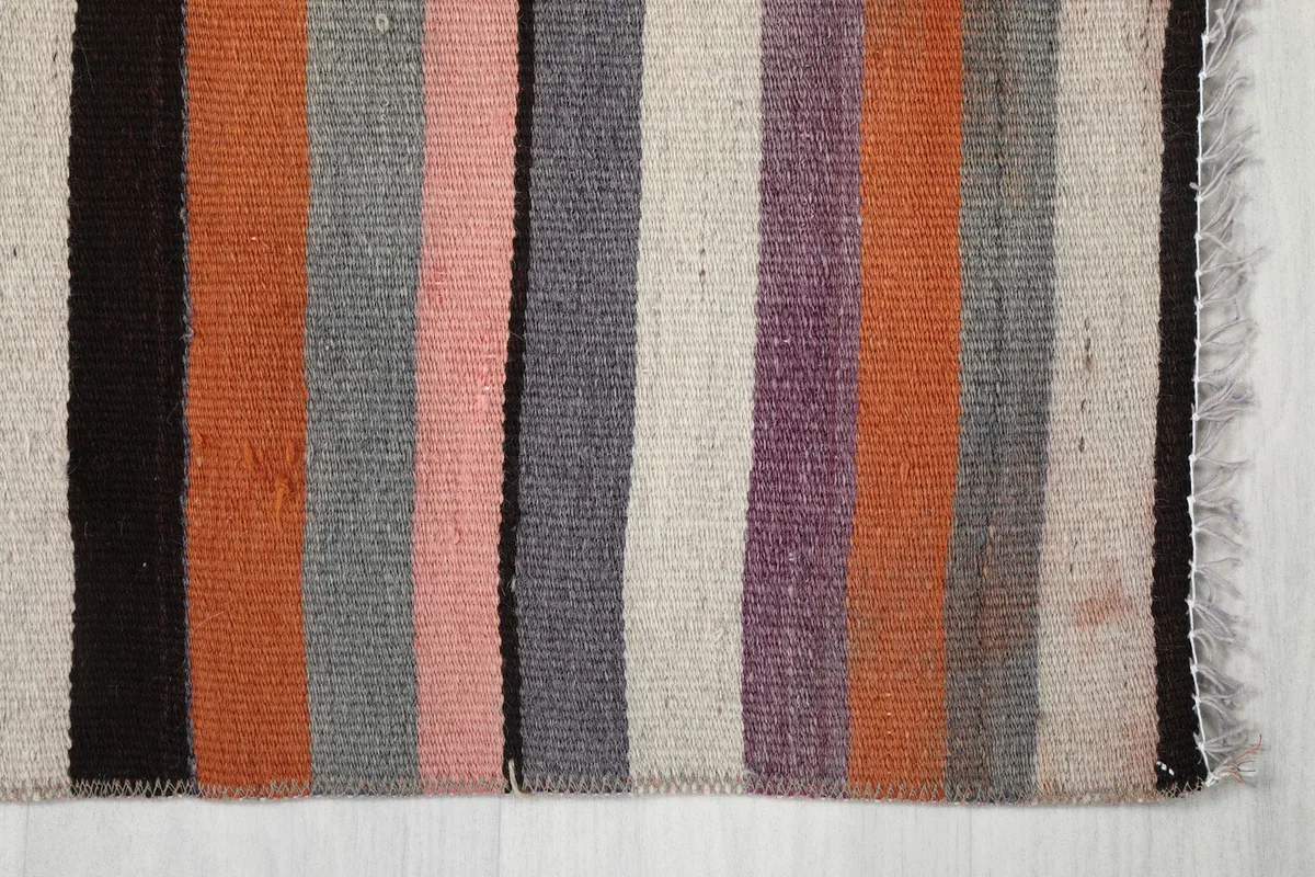 Detailed view of the rug's stripes, showing variations in pink, orange, gray, and ivory