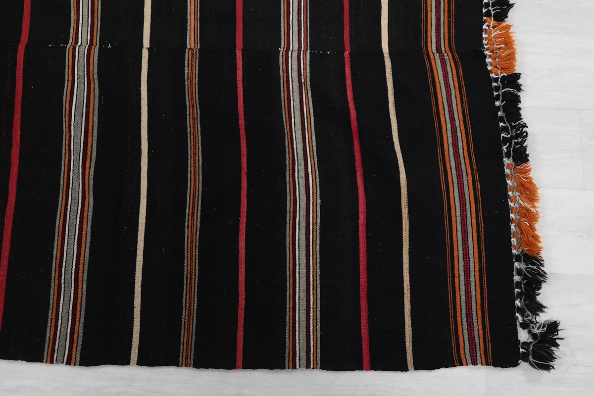 Detail view of the rug's short end, showing stripes and fringe