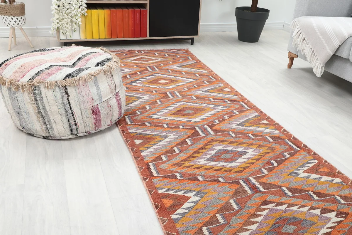 Close-up view of the rust runner rug's geometric pattern next to a textured pouf in a room setting.