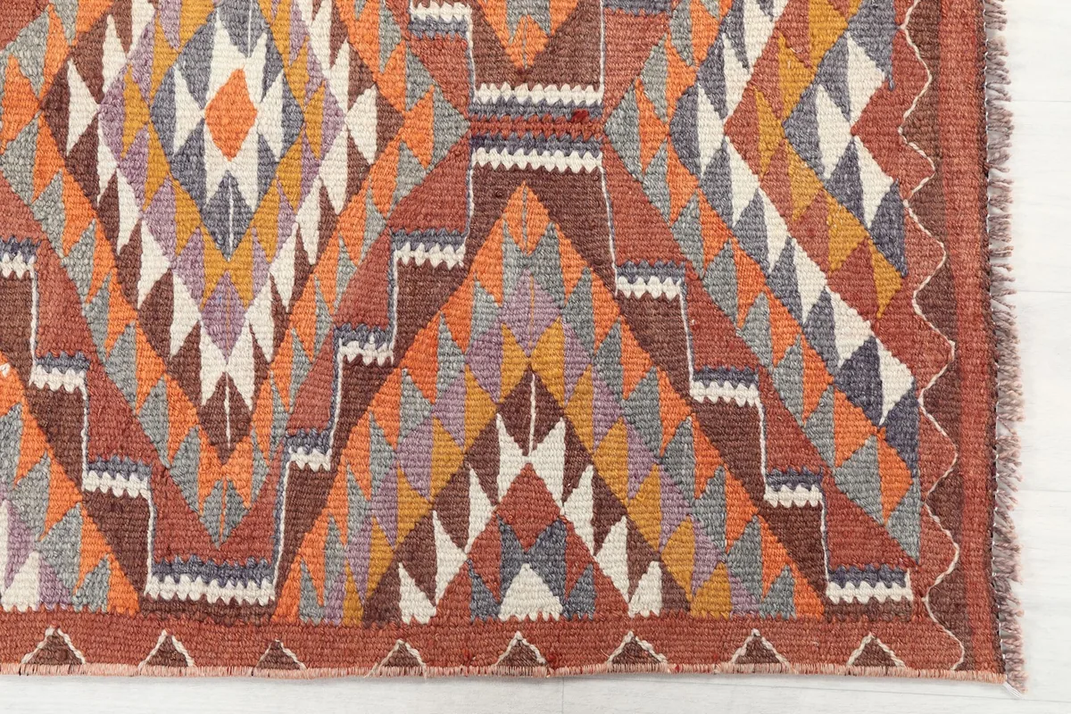 Detailed view of the rug's rust, gray, and gold geometric diamond and triangle motifs.