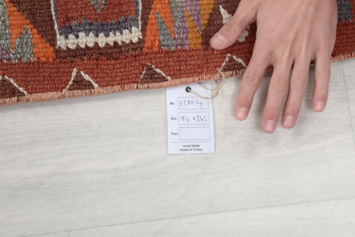 Hand next to the rug showing a tag with size 94 x 365 cm and 'Handmade in Turkey' text.