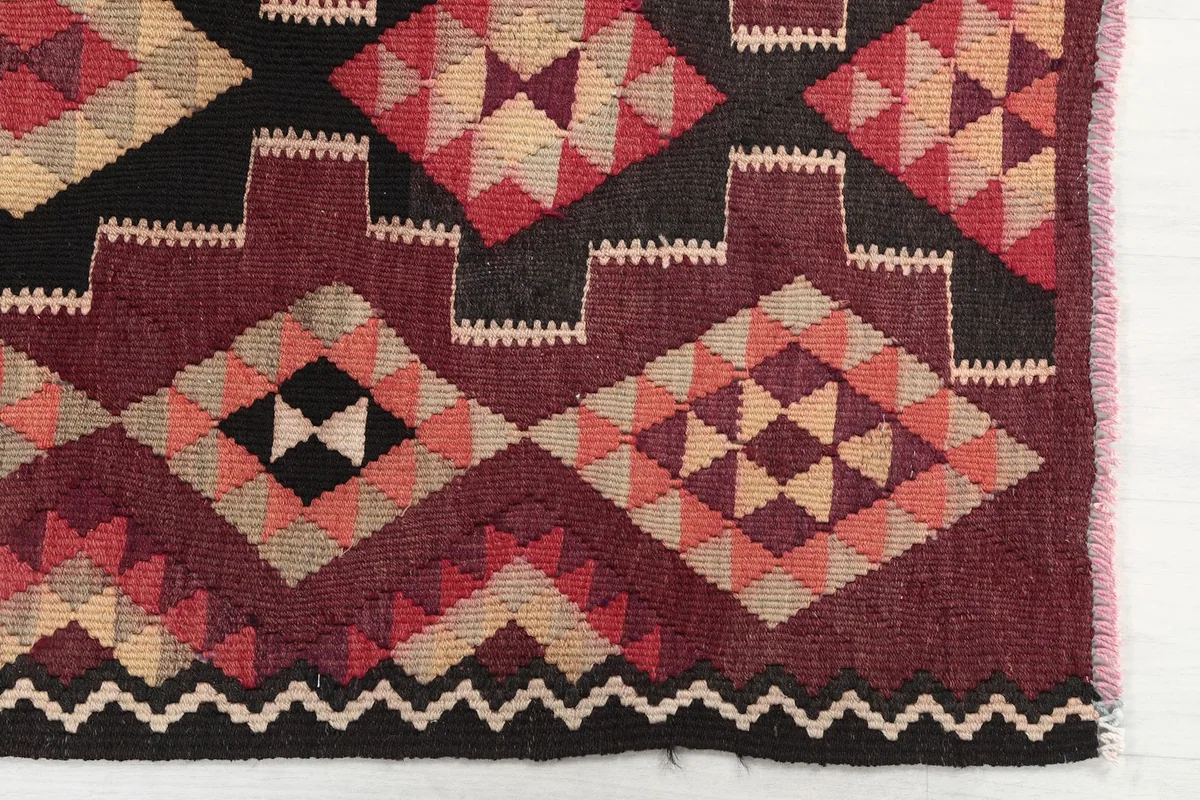 Detailed view of the hand-knotted geometric motifs in rust, black, and beige at one end of the rug