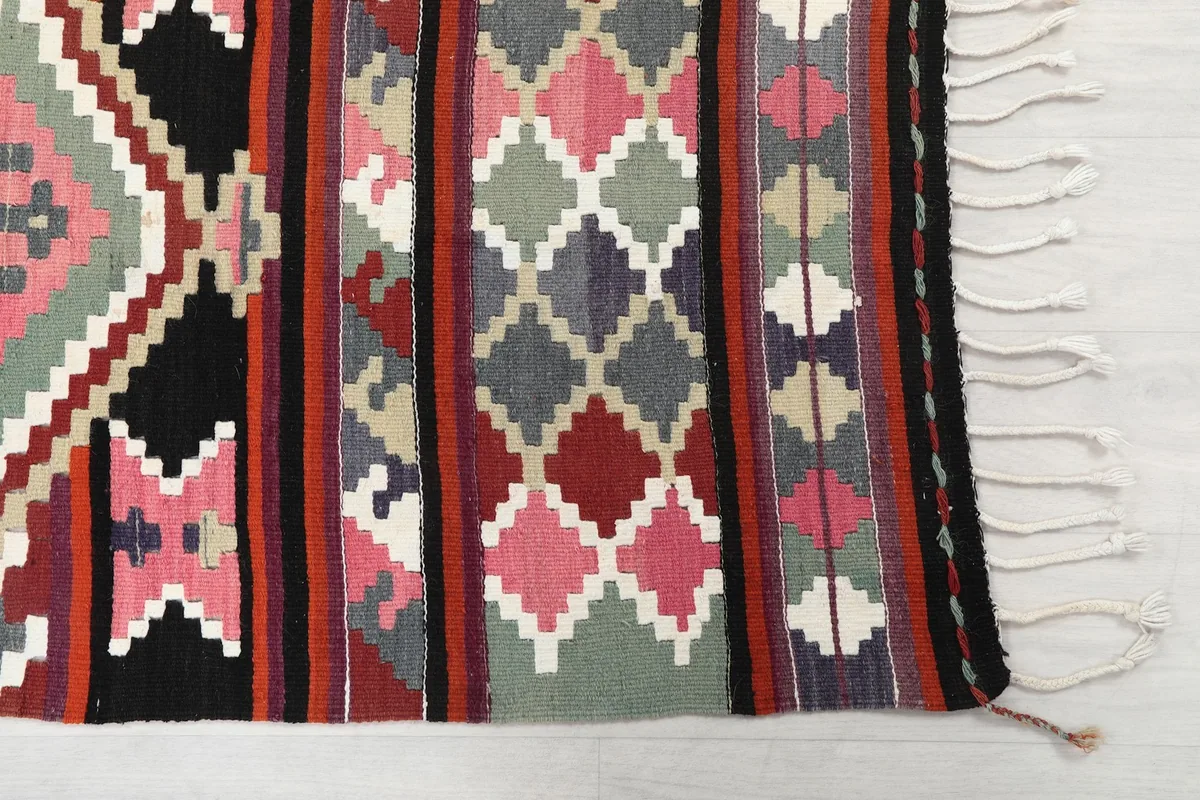 Detailed close-up of the hand-knotted pile, showing the distinct rust, pink, gray, and black geometric motifs.