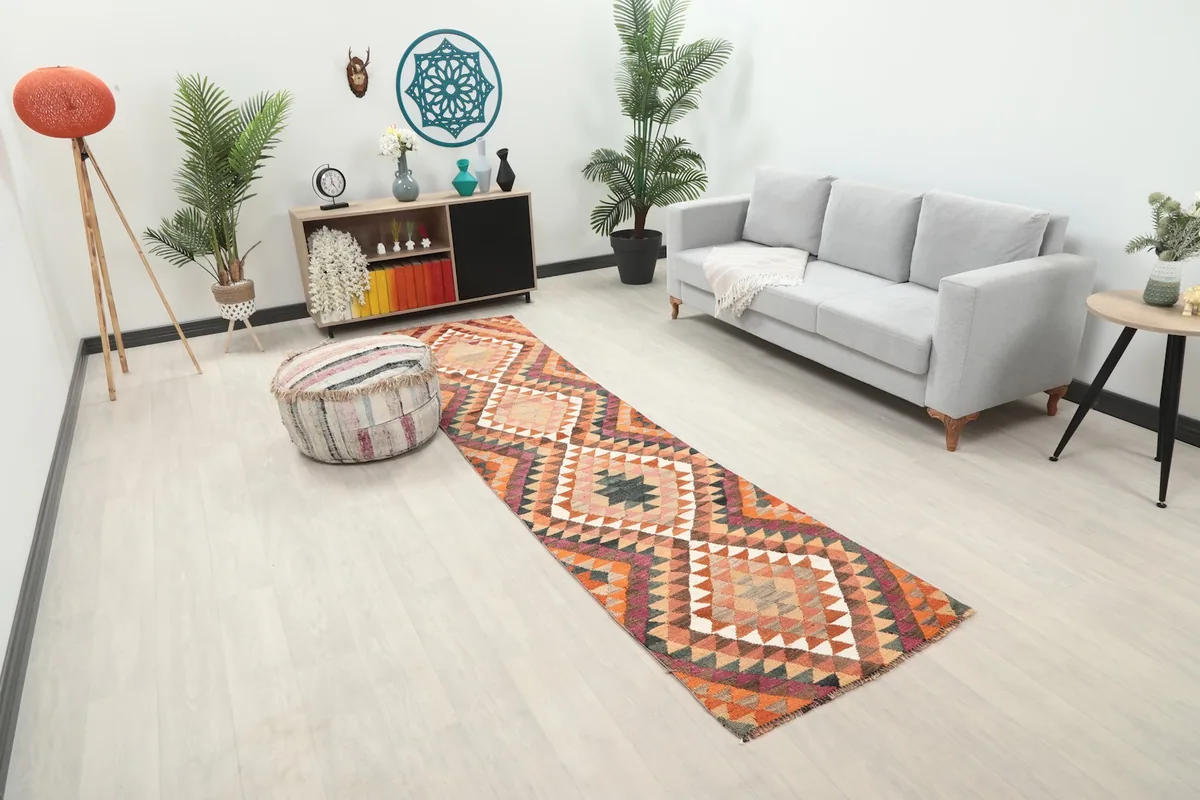 Angle view of the orange and rust runner rug in a room, highlighting its geometric pattern and texture.