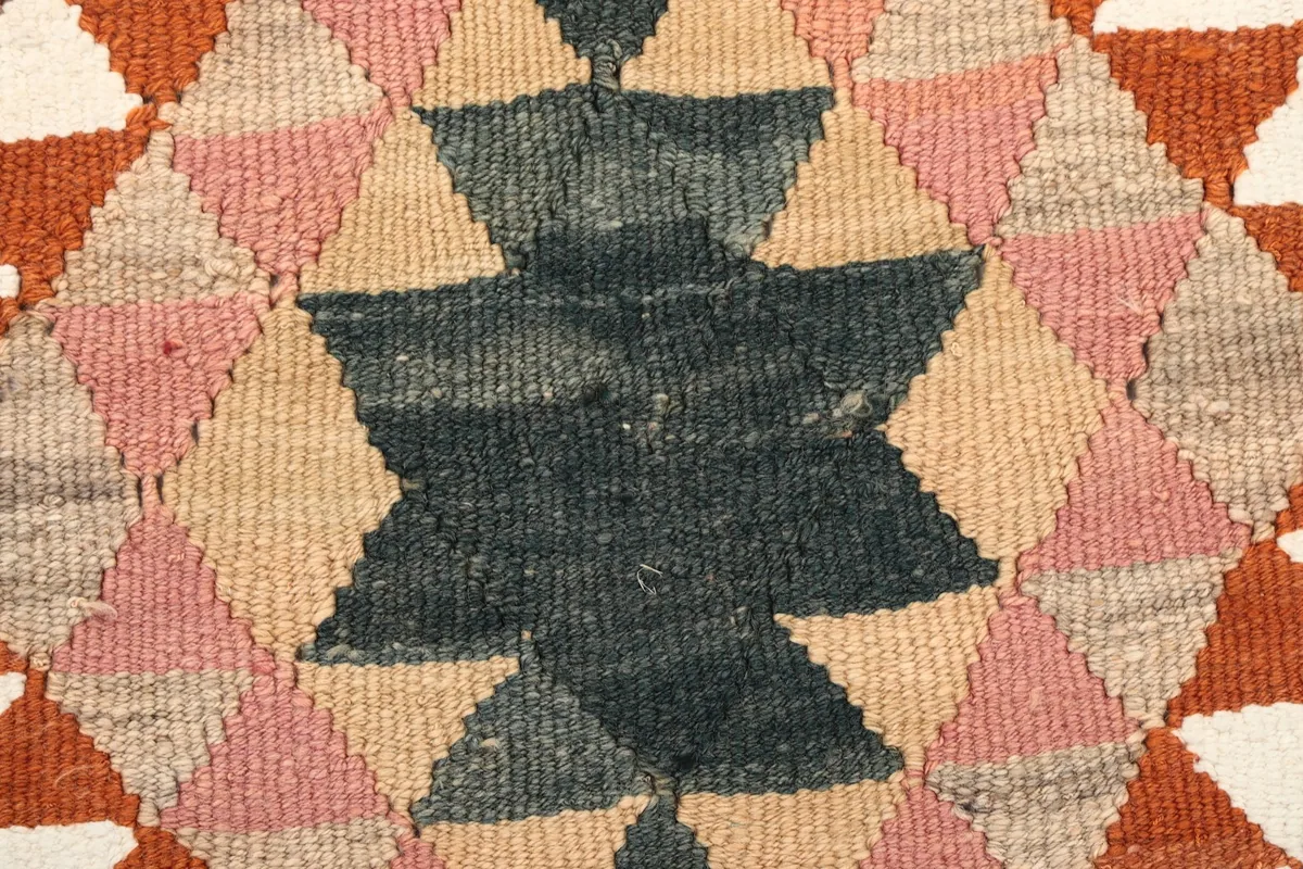 Extreme close-up of the charcoal and pink geometric motif, revealing the wool texture and knots.